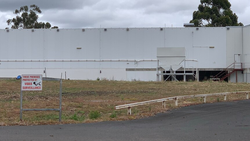Image of a white industrial building, with a sign warning trespassers to stay away out the front.