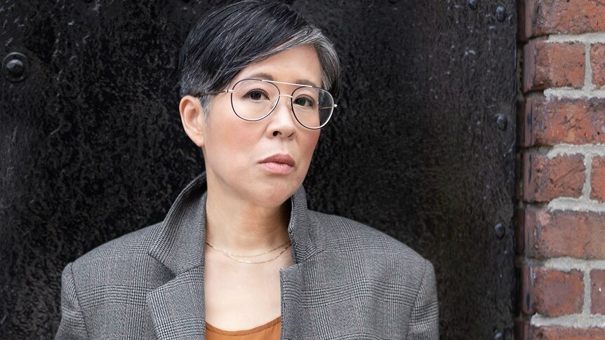 An Asian woman in glasses standing in a brick doorway