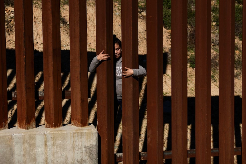 A migrant is seen holding onto the border fence