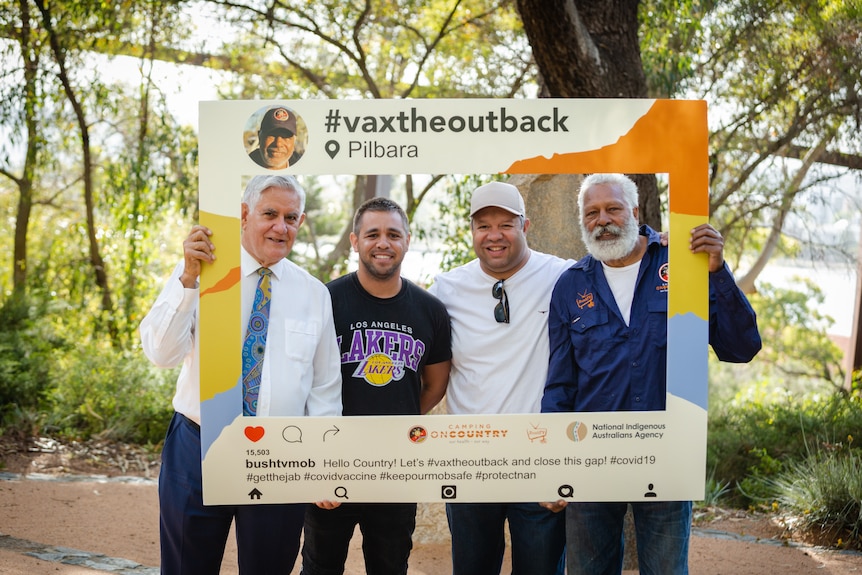Four men including Ken Wyatt and Ernie Dingo pose for a photo outdoors behind a large cardboard cut-out social media frame.