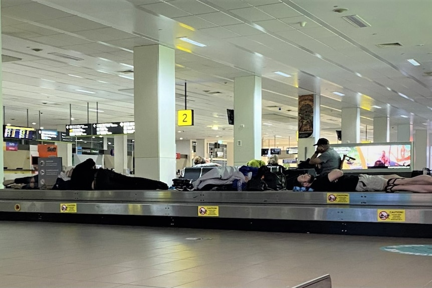 Passengers are sleeping on top of baggage carousels in an airport terminal.