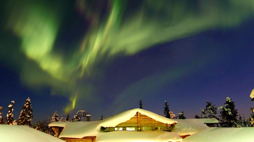 The aurora borealis above a wooden house covered in snow.