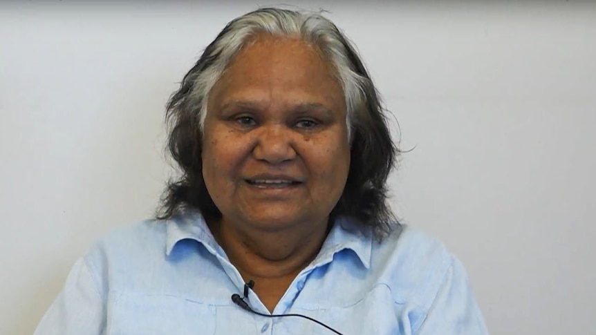 An Aboriginal woman sitting in front of a blank wall