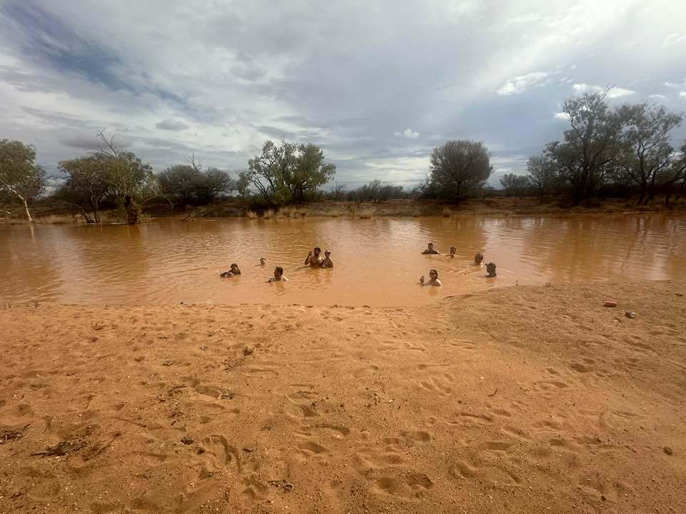 La gente nada en el agua naranja entre arena y árboles.