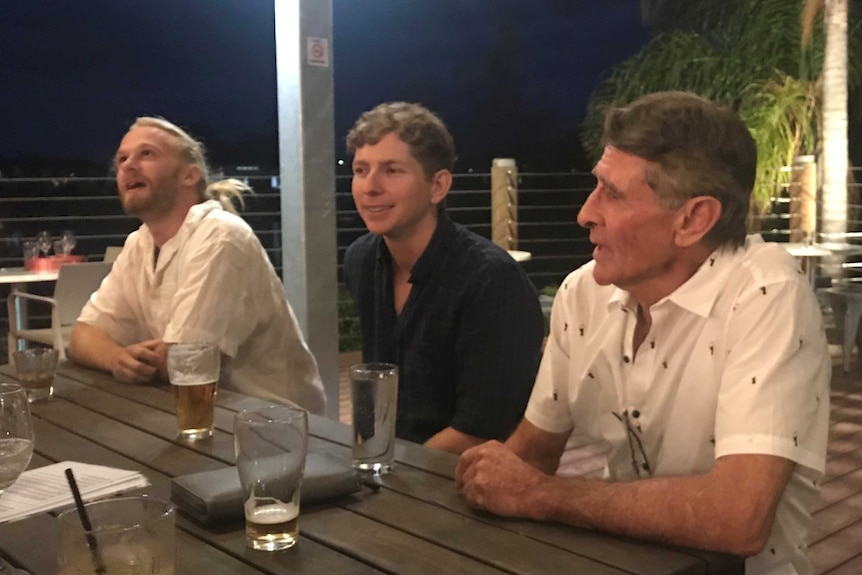 Three men sit an an outdoor table at a function venue