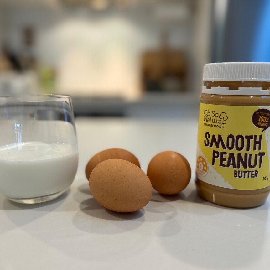 A glass of milk, eggs and a tub of peanut butter.