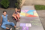 Children smile next to chalk drawings on a footpath.