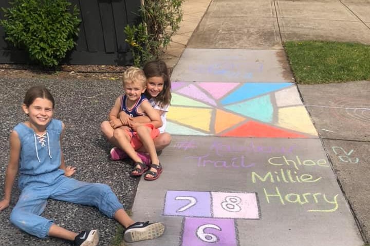 Children smile next to chalk drawings on a footpath.