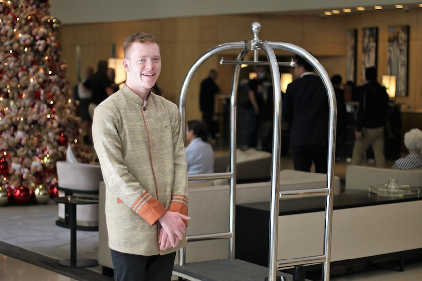 A young white man with short hair working as a bell boy in a hotel lobby 