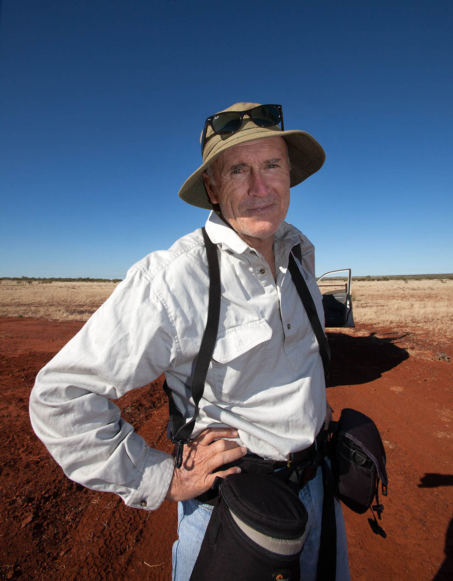 A portrait of Darwin photographer David Hancock, against a background of blue sky and red dirt.