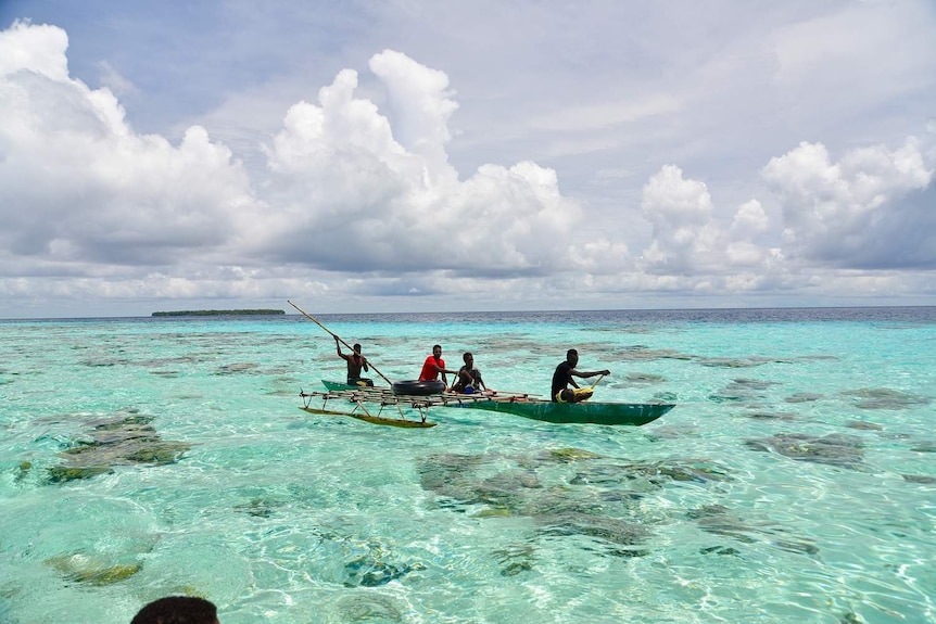 Four men row a wooden boat through crystal clear waters.