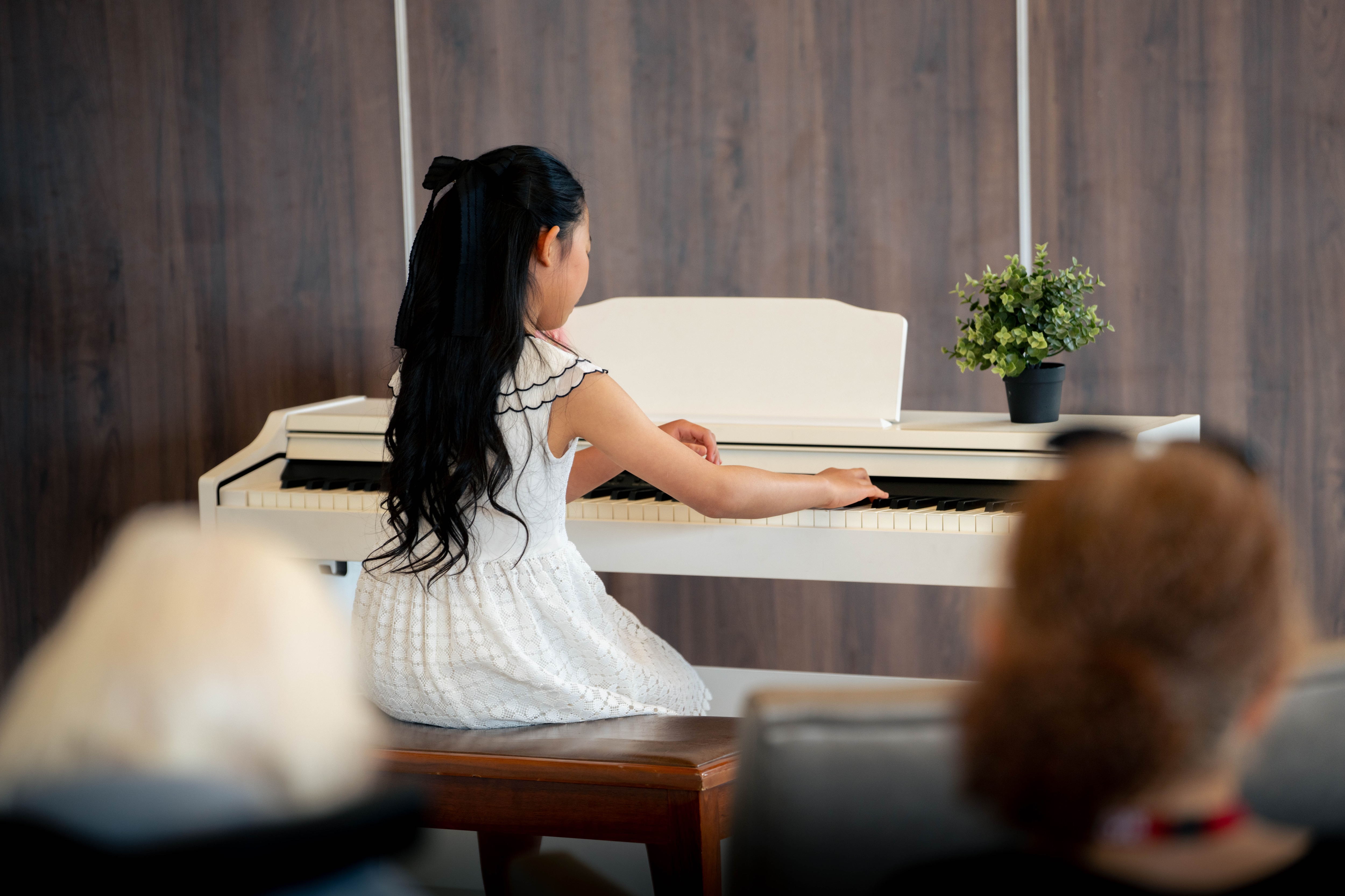 Fei, in a white dress, performs a piano piece on a white piano of aged care residents.