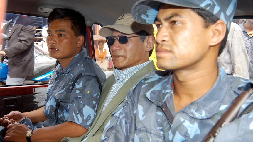 A man with a hat and sunglasses sat between two men in military uniform in a car