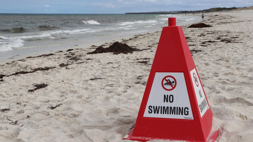 Red cone with a no swimming sign attached on a white sand beach