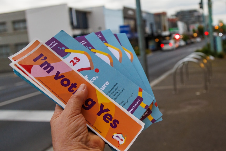 'I'm voting Yes' pamphlets are held in a hand on a street.