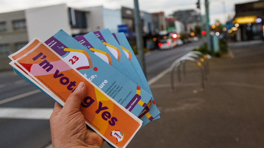 'I'm voting Yes' pamphlets are held in a hand on a street.