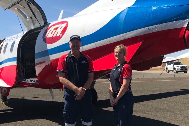 A man and a woman stand next to an RFDS plane outside, wearing blue and red shirts.