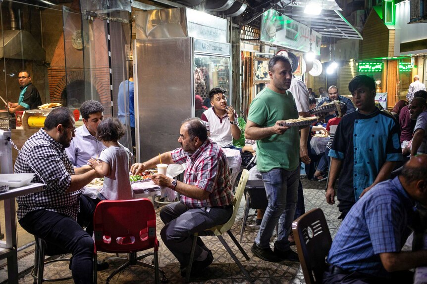 People eat food on tables in a busy street outside a restaurant.