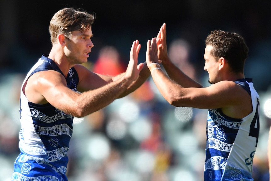 Two Geelong AFL players give each other a high five as they celebrate a goal against the Adelaide Crows.