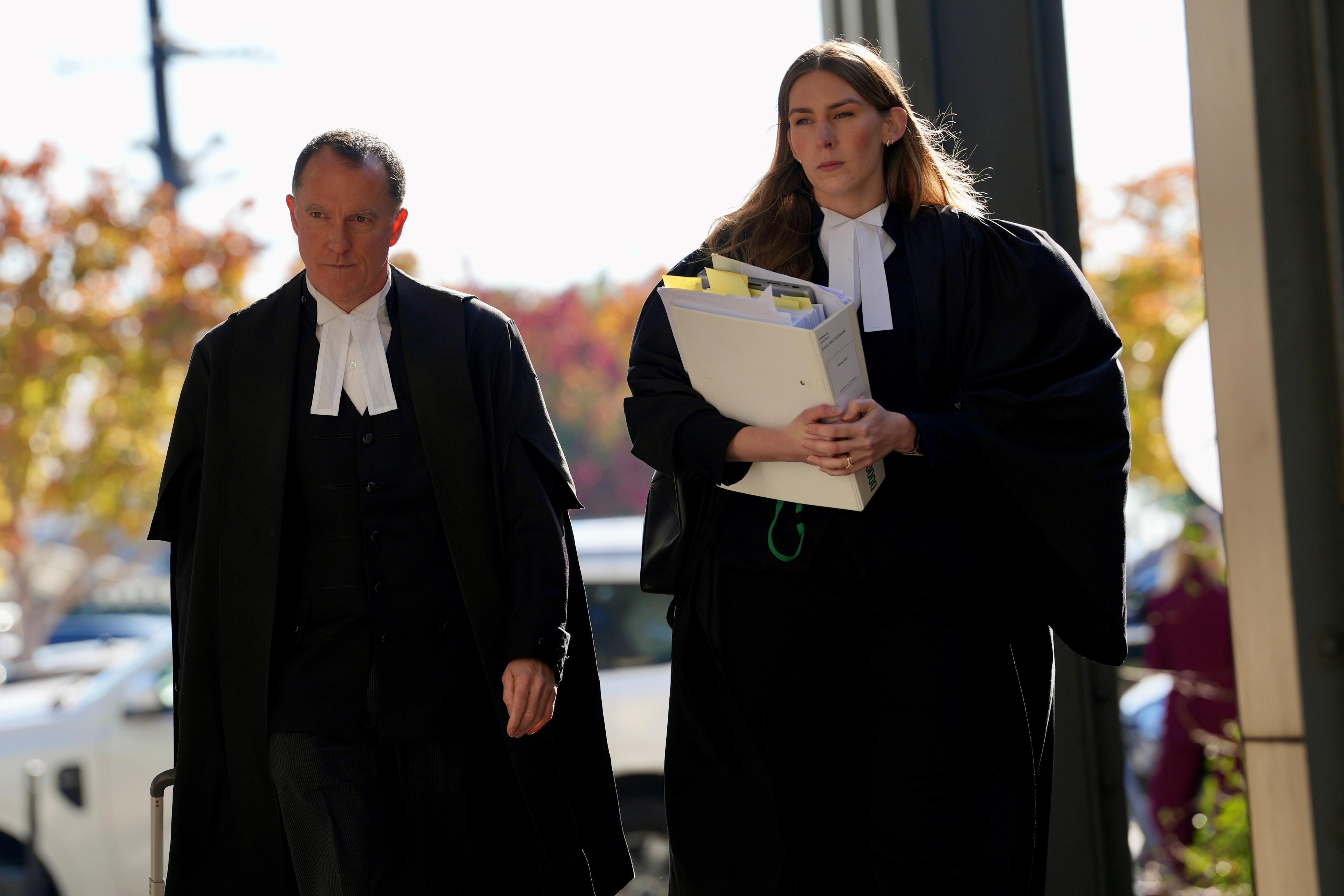 Sophie, de largo cabello castaño, bata negra y cuello blanco, camina seriamente por una calle.