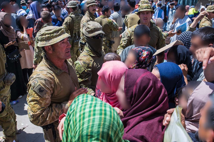 Des soldats australiens se tiennent parmi une foule de personnes, certains ont le visage flou. 