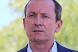 A close up of Mark McGowan wearing a blue suit, standing outside with green trees and blue sky behind him.