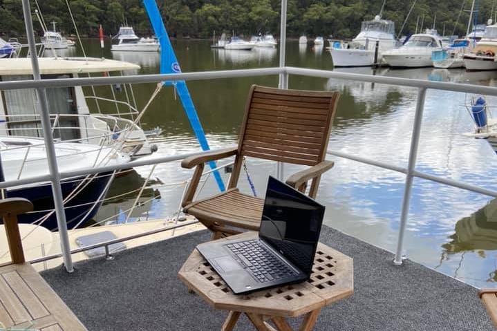 A laptop sits on a wooden table on a houseboat. The river can be seen in the background.