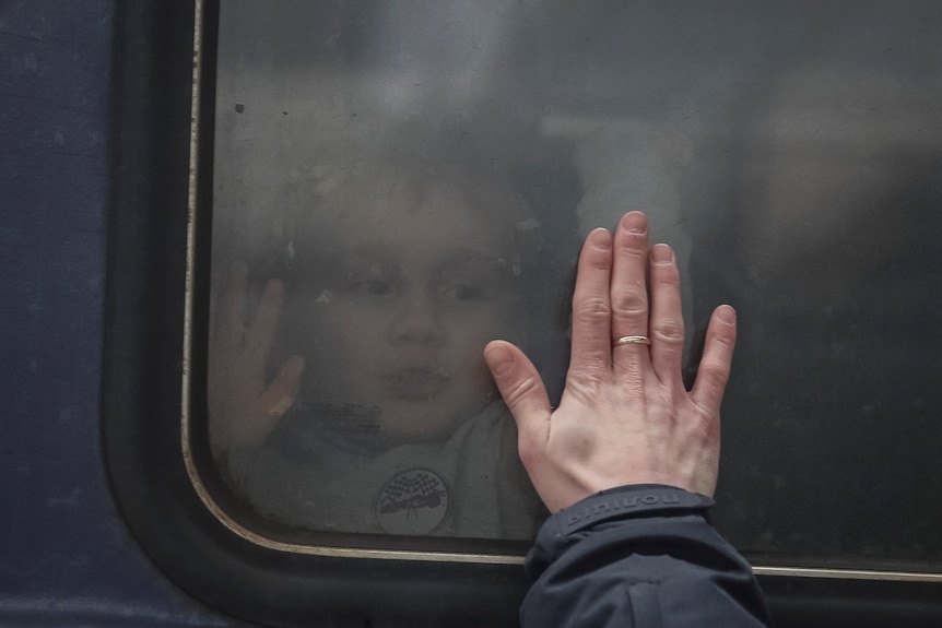 A hand up to a train window as a child peers out