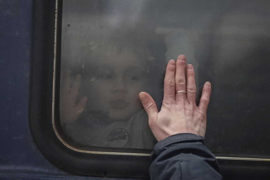 A view from outside a train as a person puts their hand onto a train window, inside which a child is sitting.