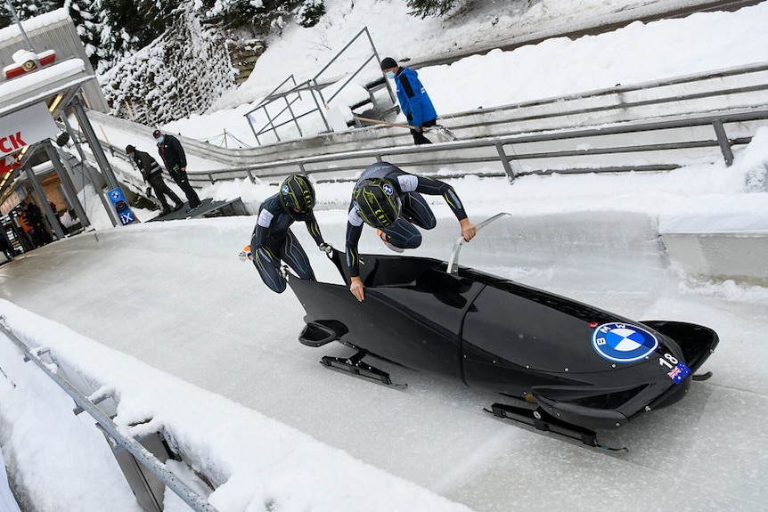 Two women are jumping into a bobsled on an ice track.