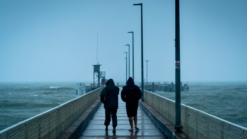 Two people walk along Palm Cove Jetty in the rain
