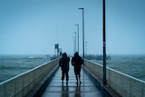 Two people walk along Palm Cove Jetty in the rain