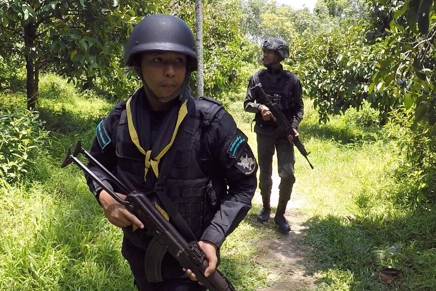 Thai security forces patrol jungle near the Malaysian border, holding guns and looking into the trees.