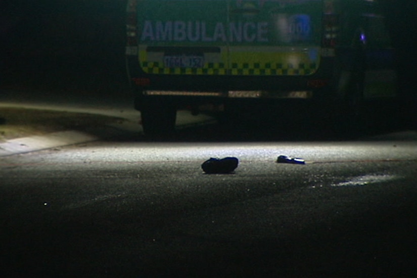 Two shoes lie on a road at night time in a spotlight in front of an ambulance.