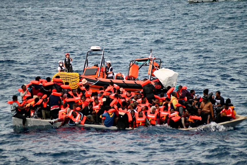 An overcrowded wooden boat packed with 99 migrants is approached by a tender of the humanitarian organization.