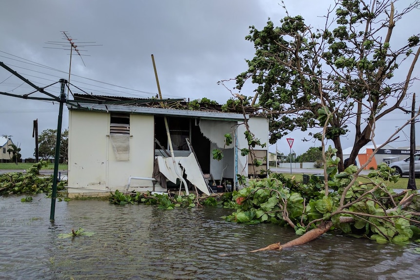 A badly damaged home surrounded by floodwaters and fallen trees