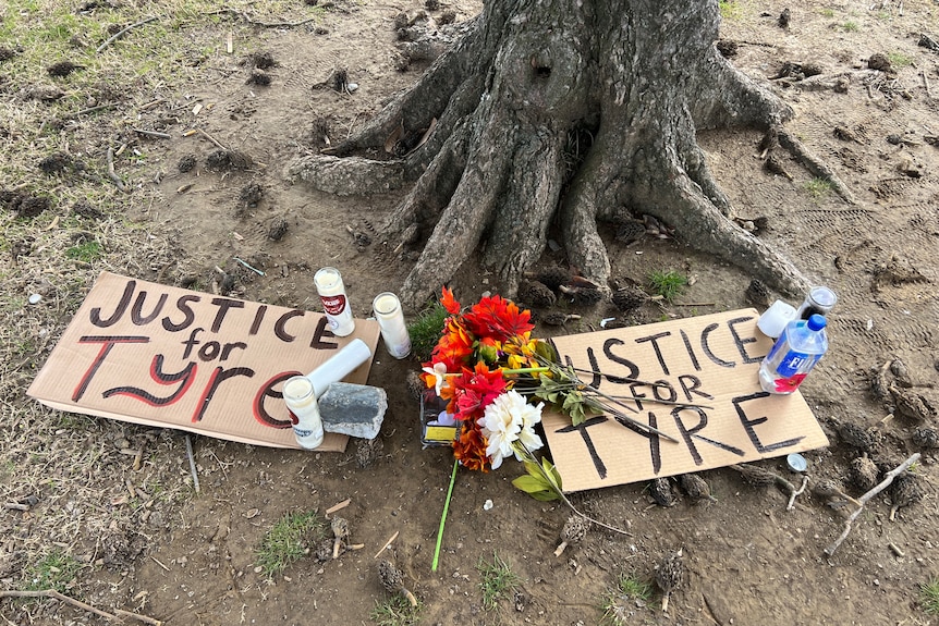 Flowers, candles and signs saying "Justice for Tyre" sit at the base of a tree. 