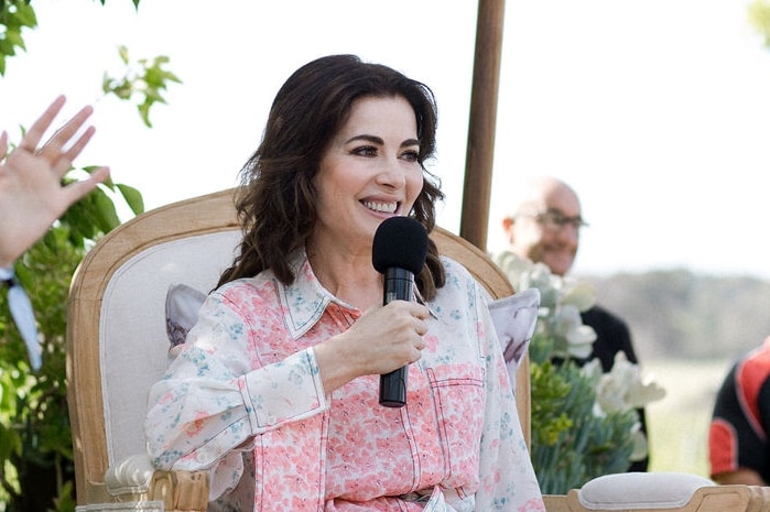 Nigella Lawson, in pink floral dress, under umbrella, holding microphone