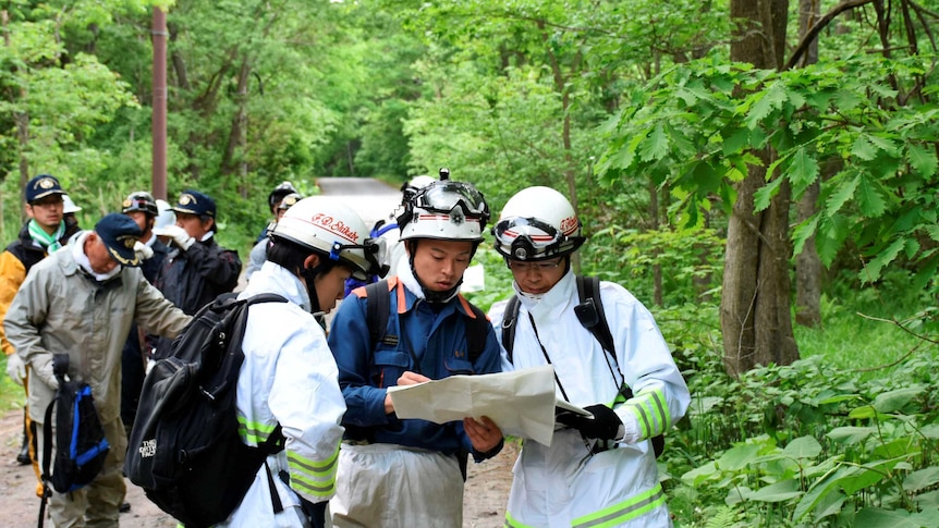 People in searching gear look at map in forest