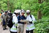People in searching gear look at map in forest