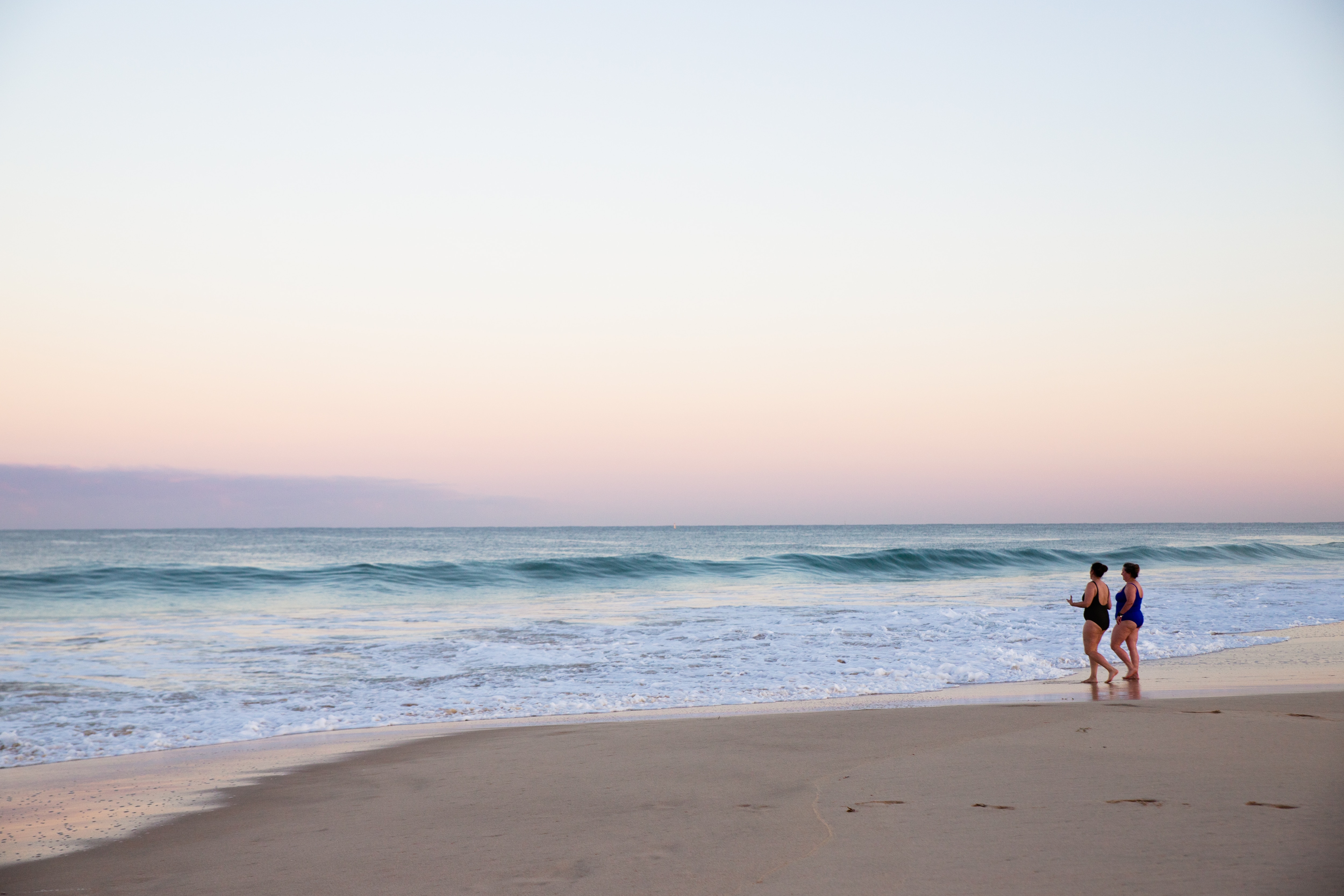 Duas mulheres caminham em direção à água ao amanhecer.