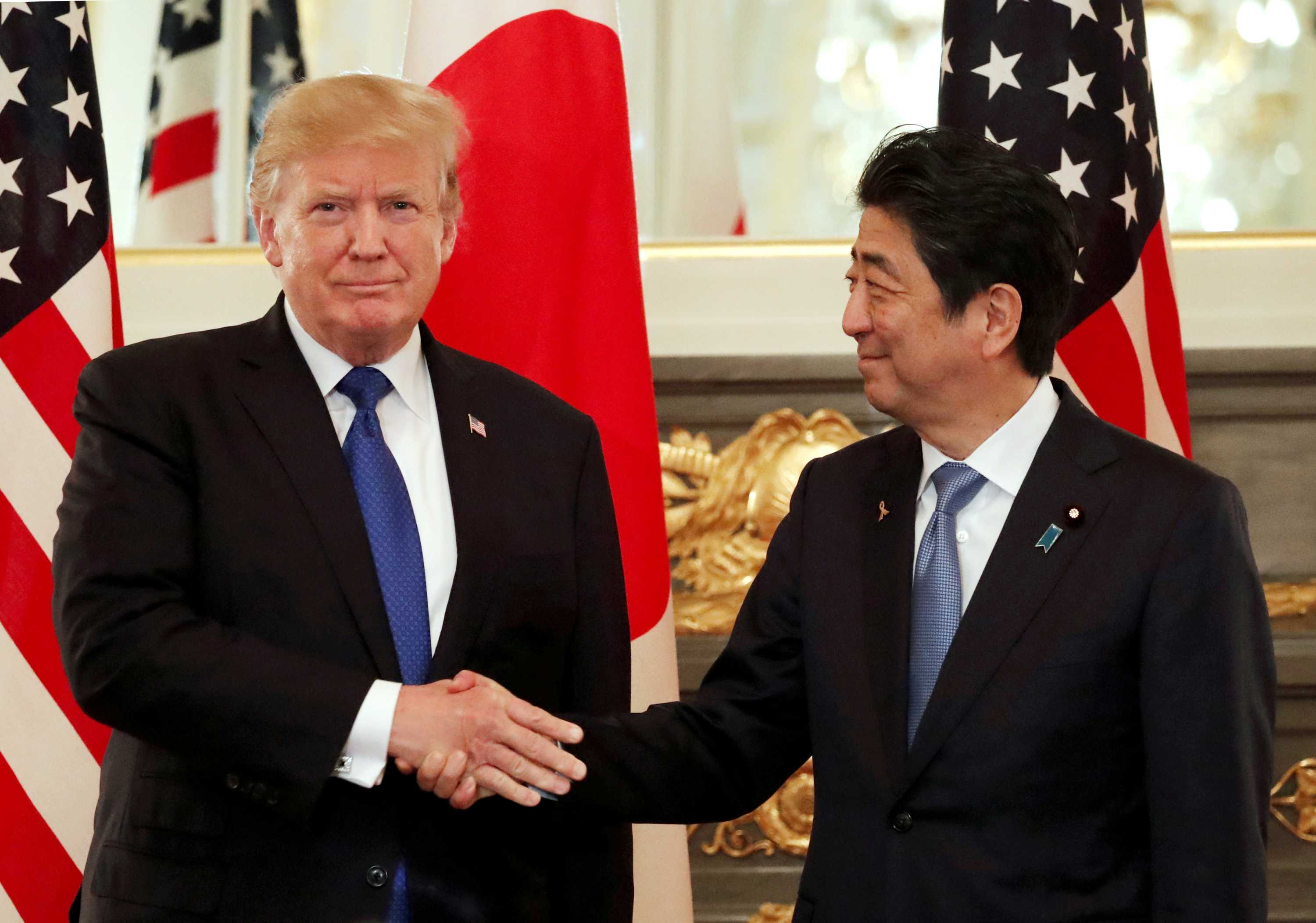 US President Donald Trump looks at the camera while shaking the hand of Japan's Prime Minister Shinzo Abe, who looks at Trump.
