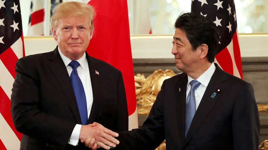 US President Donald Trump looks at the camera while shaking the hand of Japan's Prime Minister Shinzo Abe, who looks at Trump.