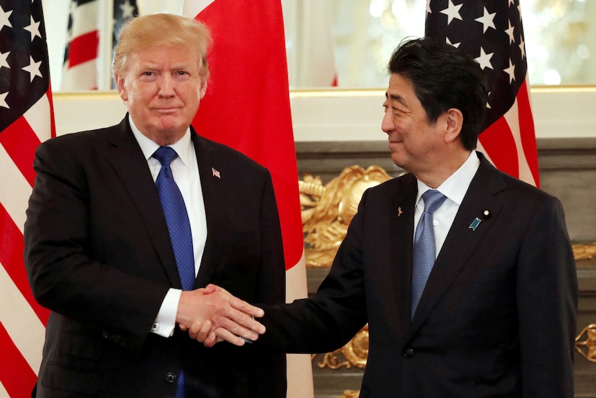 US President Donald Trump looks at the camera while shaking the hand of Japan's Prime Minister Shinzo Abe, who looks at Trump.