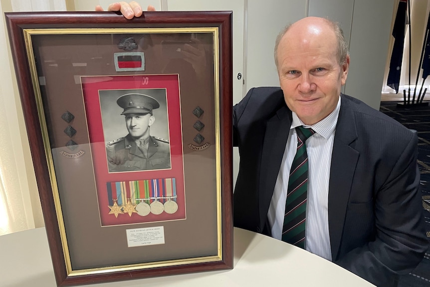L'uomo di mezza età posa con un'immagine incorniciata di un veterano di guerra e medaglie 