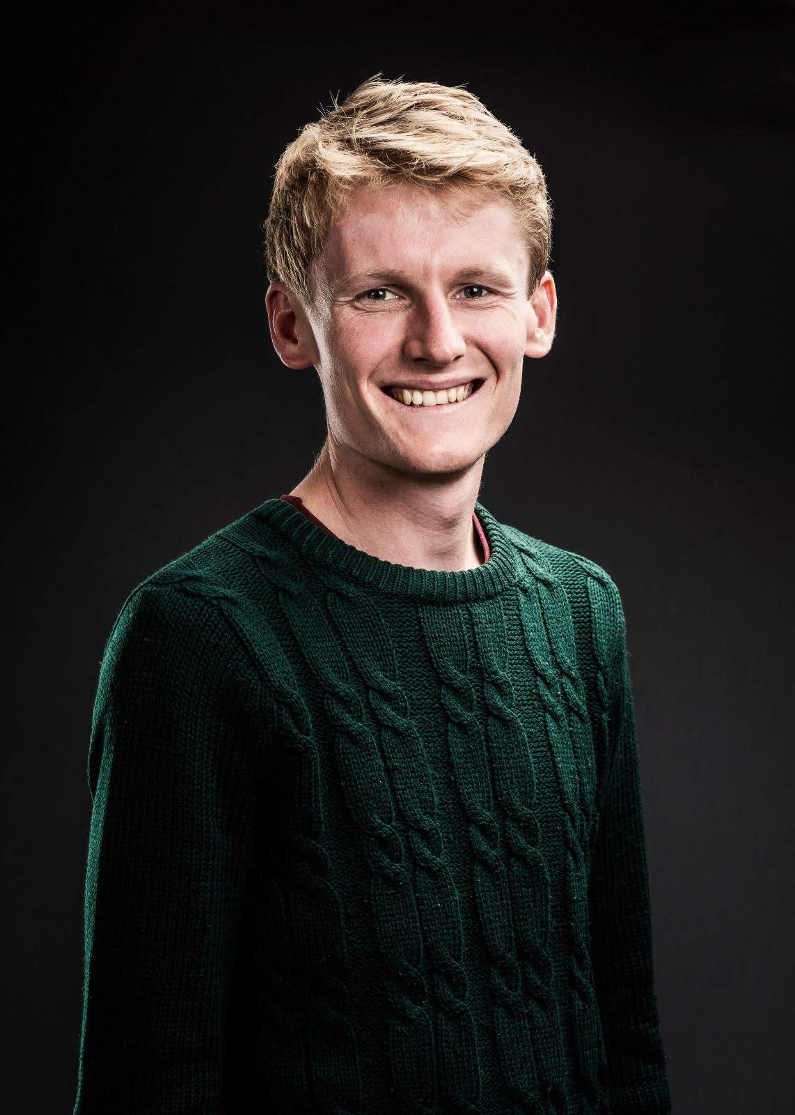 Fair haired man in a green sweater smiles at the camera 