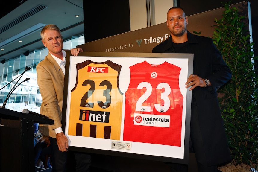AFL legend lance Franklin holds a framed picture with his Hawthorn and Sydney guernseys. 