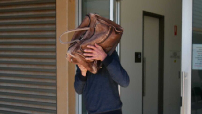 A man exits a court building with a bag covering his head and face.