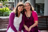 Two young women sitting on a public bench outside an office.