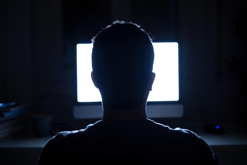 The back of a man's head is silhouetted against the glow of a bright computer screen.